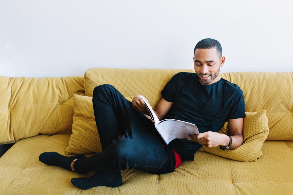 young man reading a book on couch at sober living house